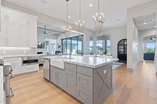 kitchen featuring dishwasher, decorative light fixtures, sink, tasteful backsplash, and a center island with sink