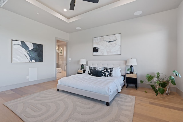 bedroom featuring ceiling fan with notable chandelier, wood-type flooring, ensuite bathroom, and a tray ceiling