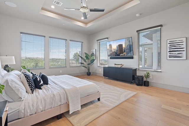 bedroom featuring ceiling fan, light hardwood / wood-style floors, and a tray ceiling