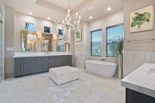 bathroom with a raised ceiling, tile walls, vanity, a washtub, and a chandelier