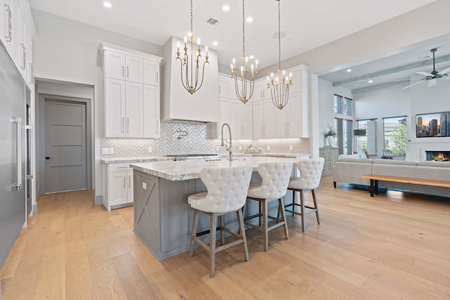 kitchen featuring stainless steel built in fridge, decorative light fixtures, white cabinetry, light stone countertops, and a center island with sink