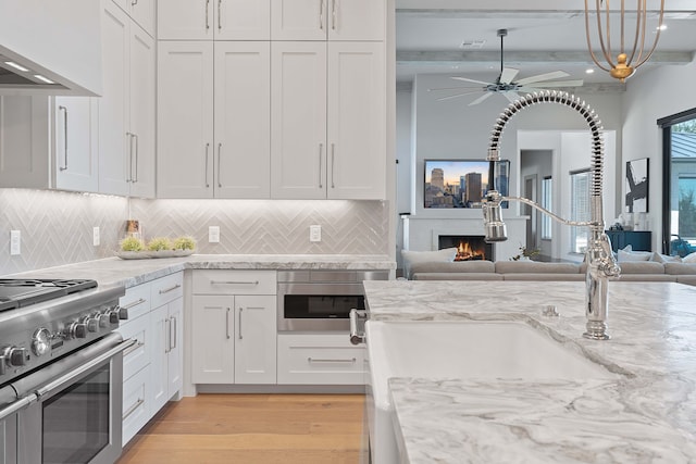 kitchen with light hardwood / wood-style flooring, white cabinets, tasteful backsplash, stainless steel range, and wall chimney range hood