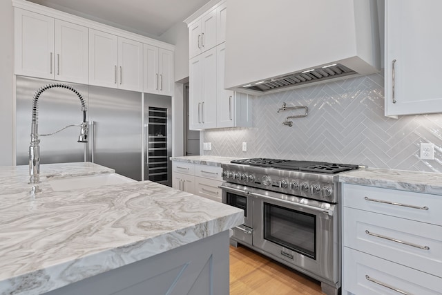 kitchen featuring sink, premium range hood, white cabinets, backsplash, and range with two ovens