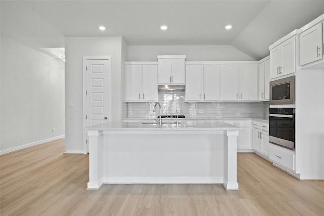 kitchen featuring stainless steel oven, white cabinets, light hardwood / wood-style flooring, decorative backsplash, and an island with sink