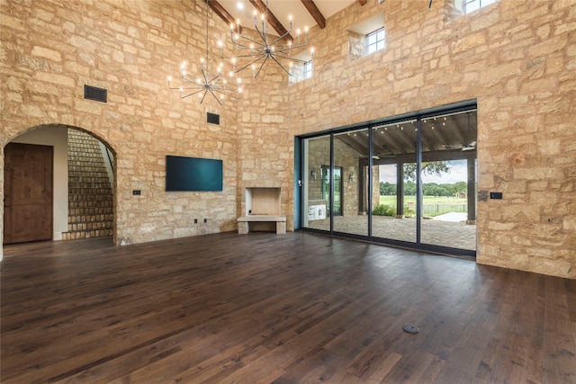 unfurnished living room featuring dark wood-type flooring, beamed ceiling, a chandelier, and a high ceiling