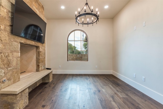 interior space featuring dark wood-type flooring, a notable chandelier, and a stone fireplace