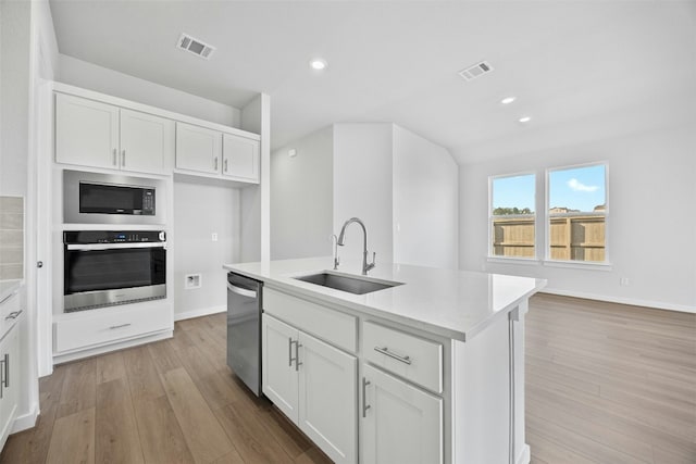 kitchen with sink, light wood-type flooring, stainless steel appliances, and a kitchen island with sink