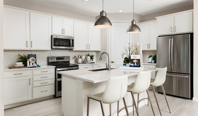 kitchen with appliances with stainless steel finishes, sink, an island with sink, and white cabinets