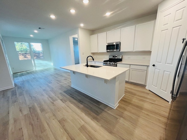 kitchen featuring stainless steel appliances, sink, a kitchen island with sink, white cabinetry, and light hardwood / wood-style flooring