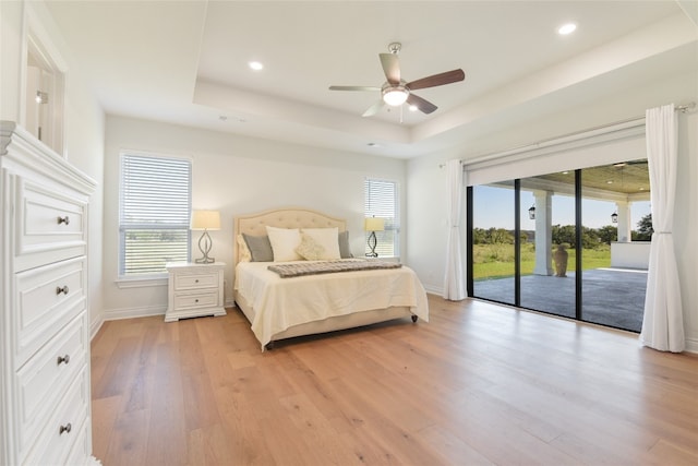 bedroom featuring access to outside, ceiling fan, light hardwood / wood-style flooring, and a raised ceiling