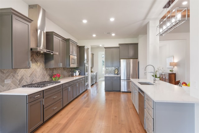 kitchen with gray cabinetry, sink, wall chimney range hood, and stainless steel appliances