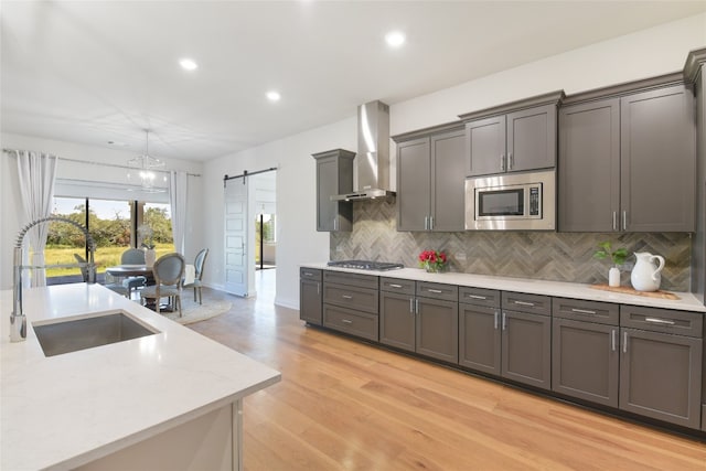 kitchen featuring sink, wall chimney range hood, stainless steel appliances, light wood-type flooring, and a barn door