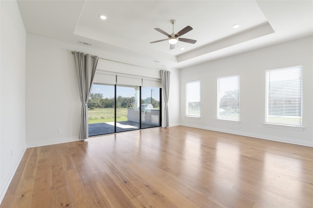 empty room with a healthy amount of sunlight, a tray ceiling, ceiling fan, and light hardwood / wood-style flooring