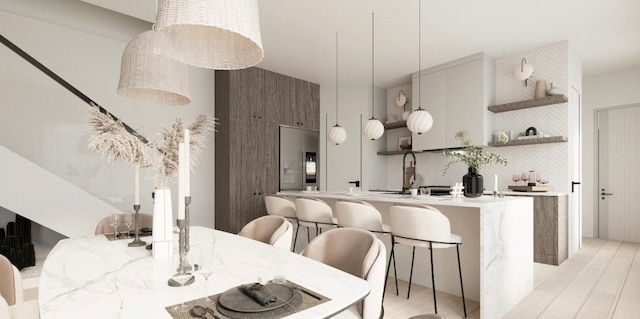 kitchen featuring a kitchen island with sink, light hardwood / wood-style flooring, built in fridge, decorative backsplash, and a breakfast bar area