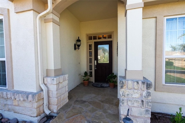 entrance to property with stone siding, covered porch, and stucco siding