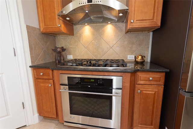 kitchen with tasteful backsplash, dark stone counters, stainless steel appliances, range hood, and light tile patterned flooring