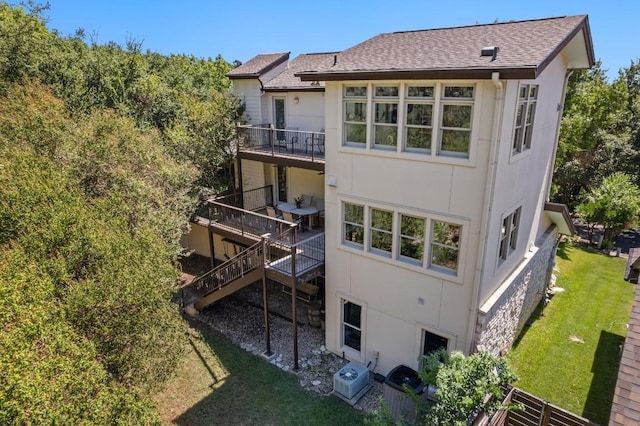 back of house featuring roof with shingles, a yard, a balcony, and stucco siding