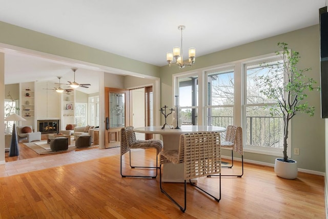 dining room with baseboards, a glass covered fireplace, lofted ceiling, and light wood-style floors