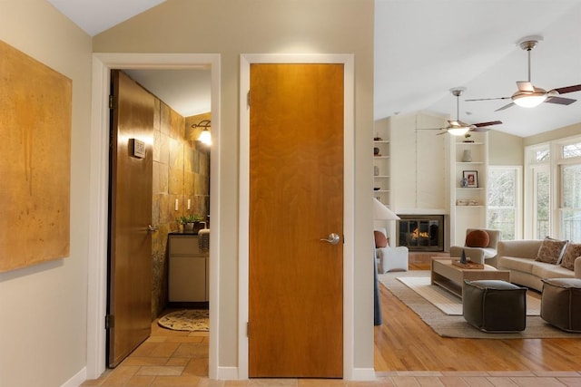 living area featuring lofted ceiling, a large fireplace, built in shelves, and baseboards