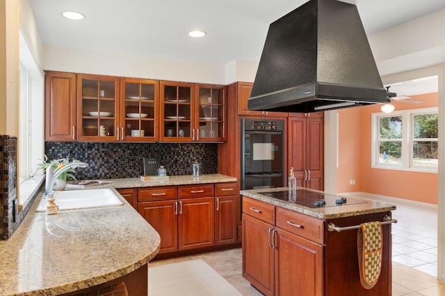 kitchen featuring glass insert cabinets, a center island, island exhaust hood, black appliances, and a sink