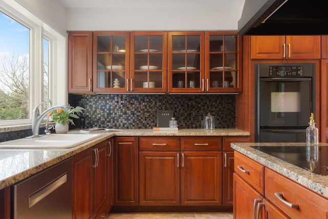 kitchen with decorative backsplash, glass insert cabinets, a sink, light stone countertops, and black appliances