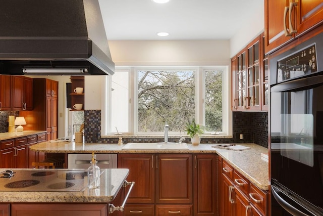 kitchen featuring glass insert cabinets, a sink, island range hood, light stone countertops, and stovetop