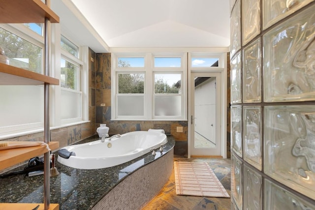 bathroom featuring a bathing tub, stone finish floor, and vaulted ceiling