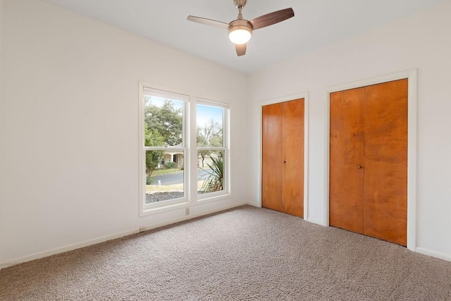 unfurnished bedroom featuring baseboards, ceiling fan, carpet flooring, and multiple closets