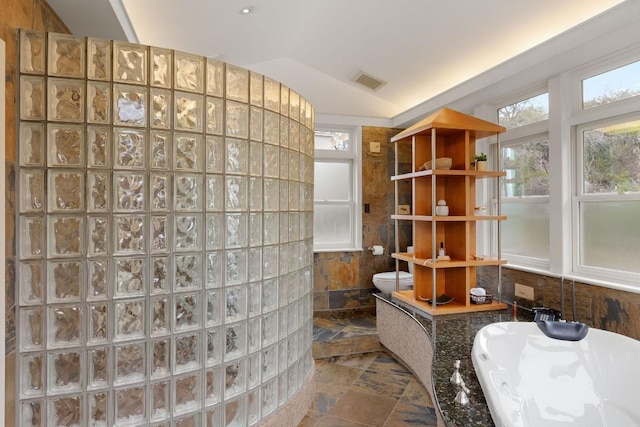 full bath with lofted ceiling, stone tile flooring, visible vents, and walk in shower