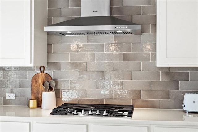 kitchen with wall chimney exhaust hood, stainless steel gas stovetop, decorative backsplash, and white cabinets