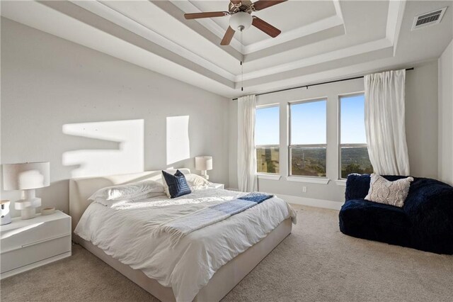 bedroom with ceiling fan, light colored carpet, and a tray ceiling