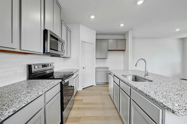 kitchen with light wood-type flooring, sink, gray cabinetry, stainless steel appliances, and light stone countertops