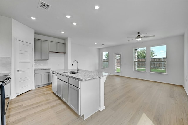 kitchen featuring an island with sink, backsplash, gray cabinets, light hardwood / wood-style flooring, and sink