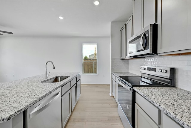 kitchen with light stone counters, sink, gray cabinetry, appliances with stainless steel finishes, and light hardwood / wood-style floors