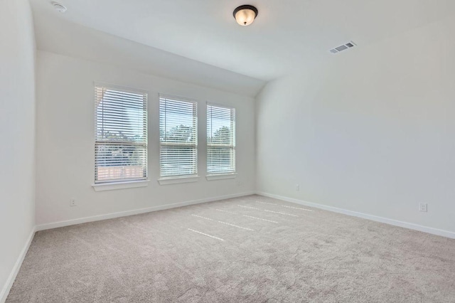 empty room featuring light carpet, baseboards, visible vents, and vaulted ceiling