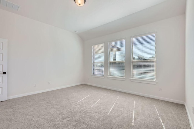 spare room featuring light colored carpet, visible vents, lofted ceiling, and baseboards