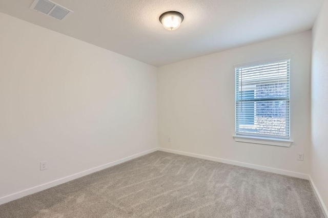 spare room with carpet floors, baseboards, visible vents, and a textured ceiling