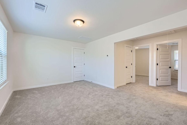 carpeted empty room with attic access, visible vents, and baseboards