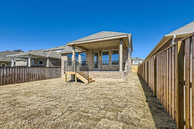 back of property featuring brick siding, roof with shingles, and a fenced backyard