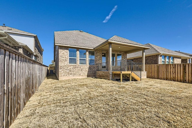 rear view of house with brick siding, roof with shingles, and a fenced backyard