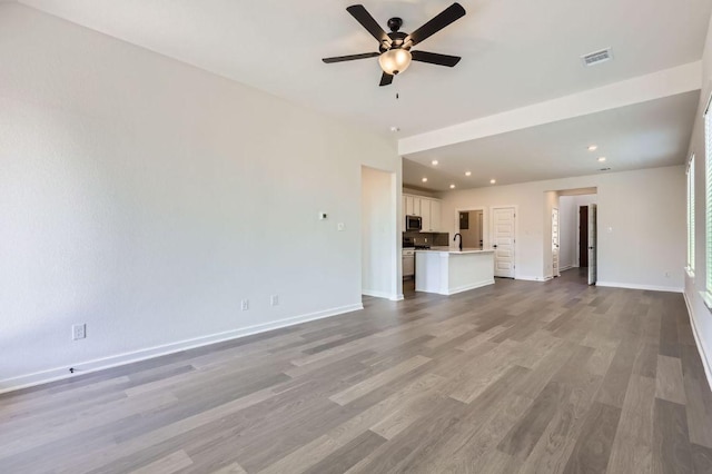 unfurnished living room featuring recessed lighting, a sink, visible vents, baseboards, and light wood-style floors