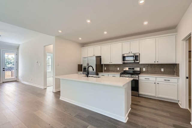 kitchen featuring stainless steel appliances, a kitchen island with sink, a sink, and tasteful backsplash