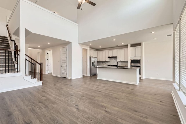 unfurnished living room featuring baseboards, dark wood-style flooring, ceiling fan, and stairs