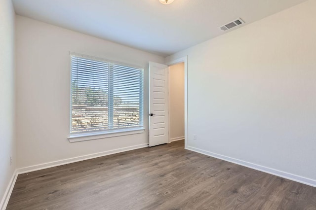 spare room featuring wood finished floors, visible vents, and baseboards