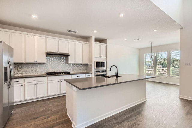 kitchen featuring visible vents, a sink, decorative backsplash, stainless steel appliances, and dark countertops