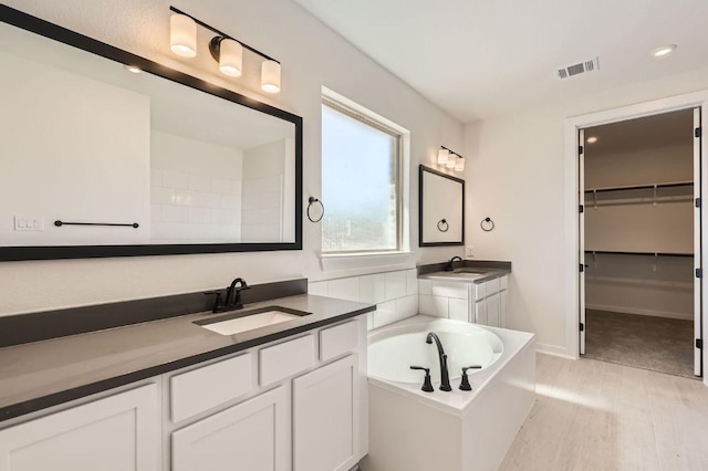 full bathroom with visible vents, a walk in closet, two vanities, a bath, and a sink