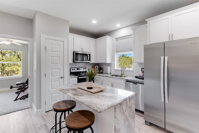 kitchen featuring a kitchen island, stainless steel appliances, sink, white cabinetry, and light wood-type flooring