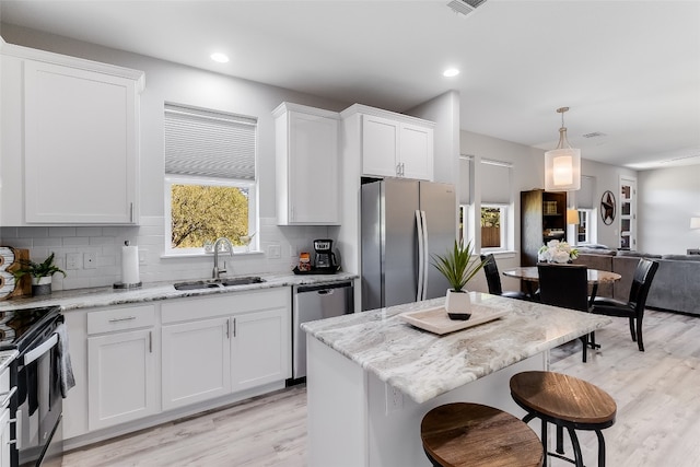 kitchen with pendant lighting, light hardwood / wood-style flooring, a center island, stainless steel appliances, and white cabinets