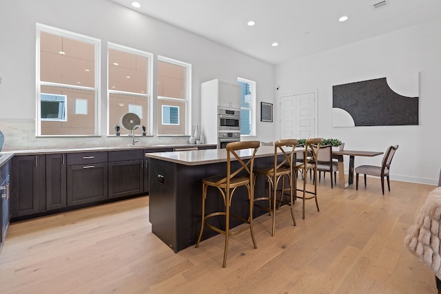 kitchen with a kitchen bar, backsplash, sink, a center island, and light hardwood / wood-style floors