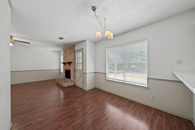 unfurnished living room with ceiling fan with notable chandelier, a fireplace, dark hardwood / wood-style flooring, and a textured ceiling